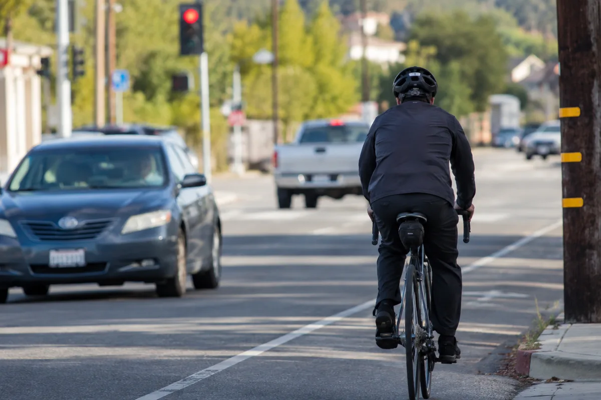 A helmeted bicyclist riding in a marked bike lane as cars share the road nearby in California